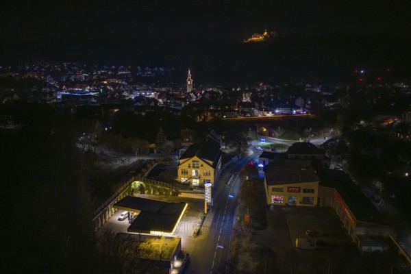 Nighttime view of city with illuminated gas station and distant castle on hill, Nagold, Calw district, Germany