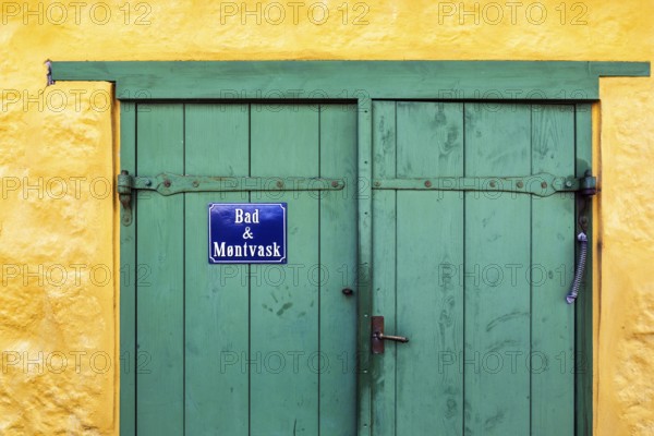 Green wooden door in a yellow wall, blue sign with inscription in Danish language, bathroom and coin laundry, laundry, ChristiansÃ¸, Christiansö, Ertholmene, Pea Islands, Bornholm, Denmark