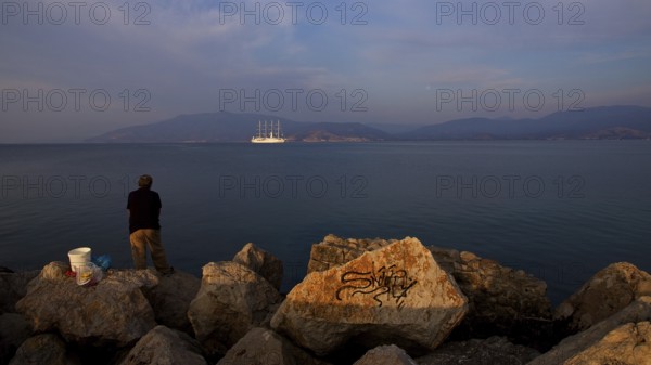 A man stands on rocks on the coast and looks at a sailing ship in the sea, Nauplion, Nafplion, Peloponnese, Greece