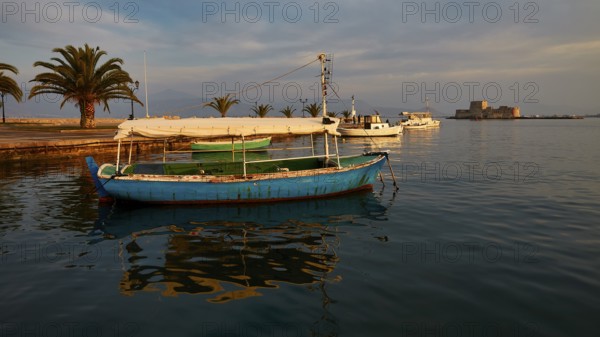 Port of Nauplion, Bourtzi island fortress, A blue boat in the harbor with palm trees and view of a castle in the evening light, Nauplion, Nafplio, Peloponnese, Greece