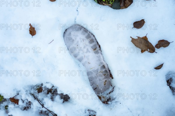 Boot tread leaving a clear imprint in the freshly fallen white snow, surrounded by scattered brown autumn leaves representing the changing seasons and outdoor exploration