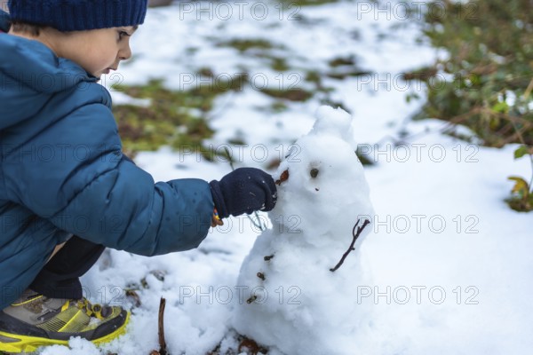 Young boy playing in the snow, carefully placing a small natural element on a snowman he is building, representing childhood creativity and winter fun