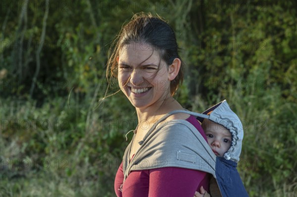 Young mother carrying her baby in a shawl on her back, Othenstorf, Mecklenburg-Western Pomerania, Germany