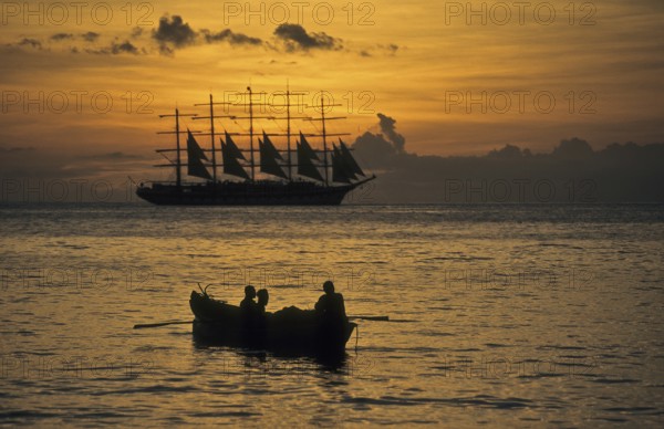 Romantic view of the Caribbean Sea during sunset In the foreground small fishing boat with three local fishermen heading out to sea for fishing at dusk, tall ship five-master sailing ship Royal Clipper, Caribbean