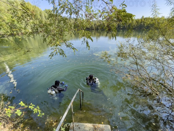 Recreational divers with diving equipment Diving tanks swim near the shore on the water surface of a small lake, Germany