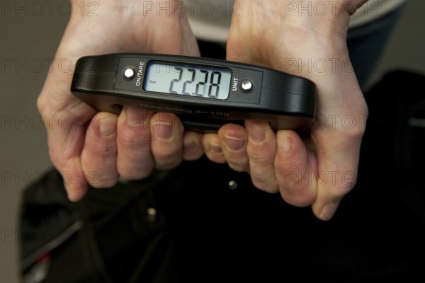 Woman holding hand scale for weight of suitcase travel bag flight luggage checks luggage weight for excess luggage weight in front of flight travel, scale shows 22.28 kg kilos, international