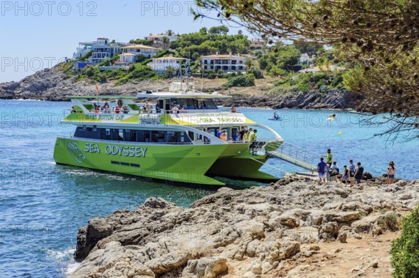 Tourists get on board a glass-bottom boat docks at the small bay Font de Sa Cala on the east coast of the Balearic island of Majorca in the Mediterranean Sea, Majorca, Balearic Islands, Spain