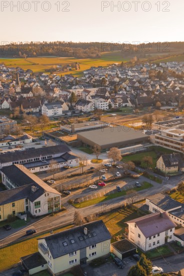 Aerial view of a suburb with buildings and roads in warm sunset light and surrounding hills, Althengstett, Calw district, Germany