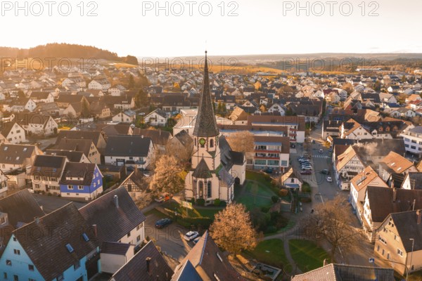 Aerial view of a village with church and autumn trees in soft sunset light, Althengstett, Calw district, Germany