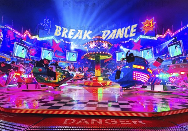 People in the colorful illuminated break dance ride at night at the All Saints Fair, Soest, North Rhine-Westphalia, Germany