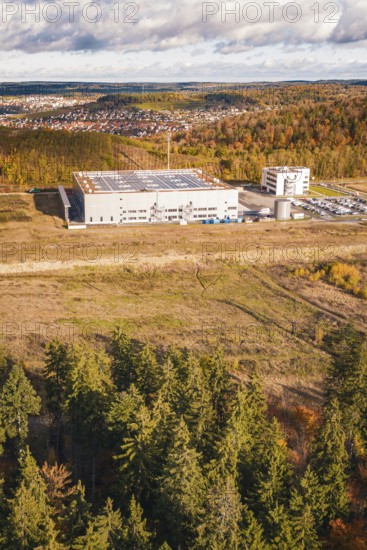 Factory building next to forest and clearing, behind a village on a hill in autumn tones, new Lindenrain industrial park, Calw, Black Forest, Germany