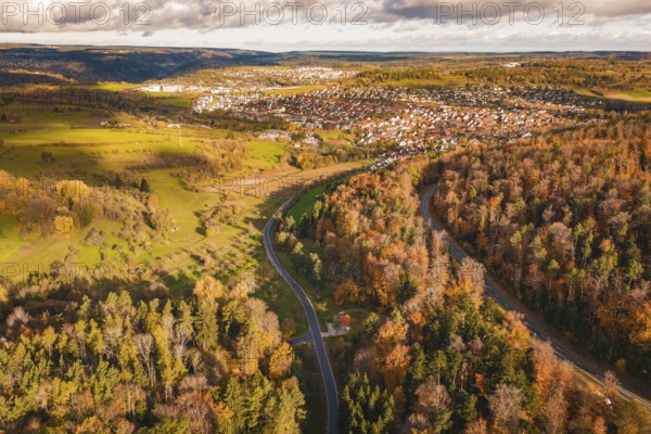 Colourful autumn landscape with a road leading through a village in hilly terrain, under a cloudy sky, new Lindenrain industrial park, Calw, Black Forest, Germany