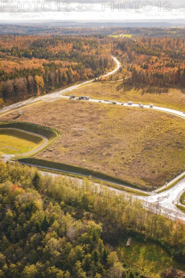 Autumn forest landscape crossed by a road next to a harvested field in sunlight, new Lindenrain industrial park, Calw, Black Forest, Germany