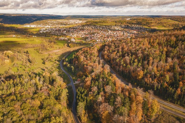 Autumn landscape from the air with colorful forest and city on the horizon under cloudy sky, new Lindenrain industrial park, Calw, Black Forest, Germany