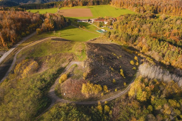 Hilly autumn landscape with colorful trees and fields, farm and winding paths, new Lindenrain industrial park, Calw, Black Forest, Germany