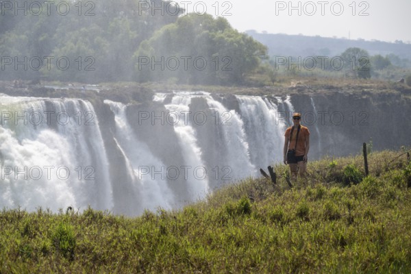 Tourist looking at waterfalls, water plunging into the depths, Victoria Falls, Zimbabwe