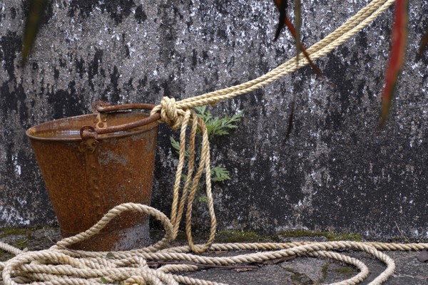 A rusted bucket and rope in front of a weathered well wall, Peermade, Kerala, India