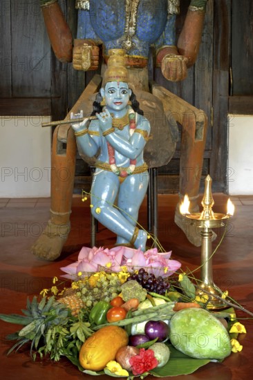 Sculpture of shepherd god Krishna playing his flute, fruits and vegetables lying on the ground, burning oil lamp, Thanksgiving, Heritage Hotel Privacy, Lake Vembanad, Kerala, India
