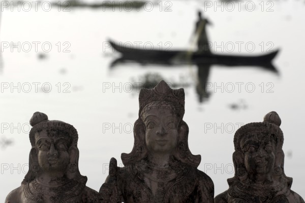 Three Hindu god statues made of clay, fishermen in a boat in the background, Vembanad Lake, Kerala, India