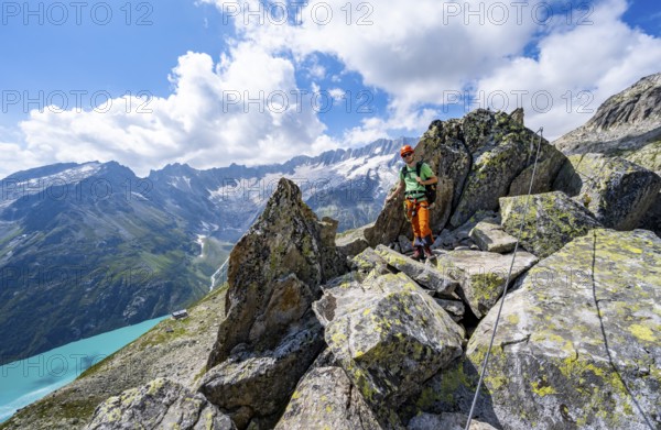 Mountaineers between boulders on the secured via ferrata Crocodile Mountain Lake at Bergseeschijen-Vorbau, view of dam glacier and dammastock, Göscheneralp, Canton of Uri, Switzerland
