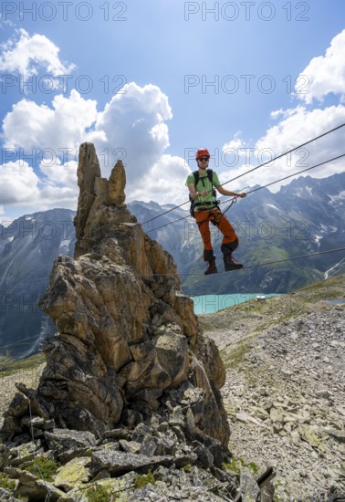 Crocodile rock formation, mountaineer on rope bridge in the Crocodile Mountain Lake via ferrata on Bergseeschijen-Vorbau, Göscheneralp, Canton of Uri, Switzerland