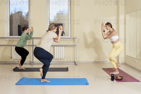 Three women are engaged in a yoga session in a calm and bright studio. They are practicing different poses on colorful mats
