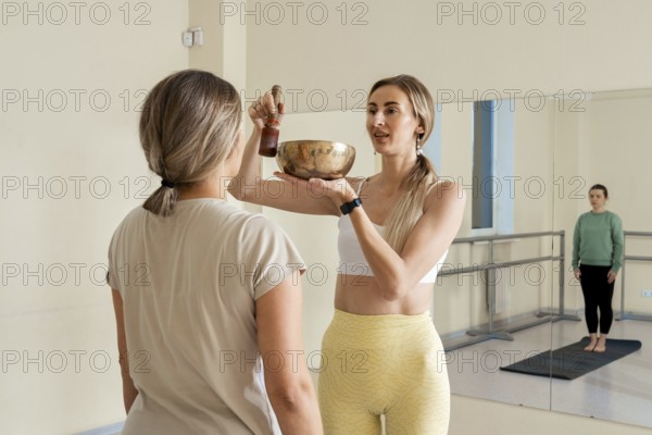 In a peaceful studio, a wellness guide holds a singing bowl while offering a sound therapy session. The participants are engaged in a calming experience that promotes relaxation and mindfulness