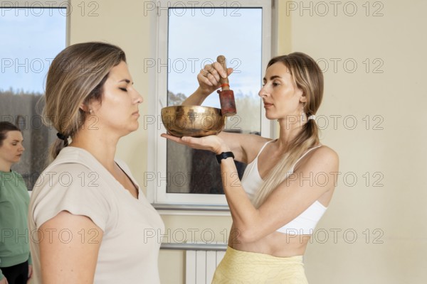 In a calm studio, a practitioner holds a singing bowl above a participant's head, creating soothing sounds