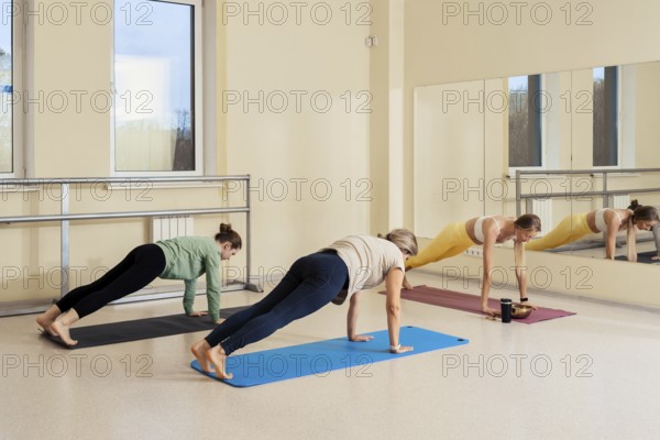 Three women are engaged in plank exercise routines in a fitness studio filled with natural light
