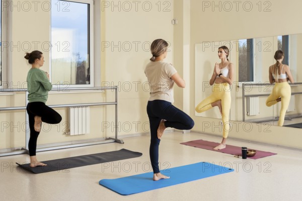 Three women practice yoga in a well-lit studio, showcasing various poses that emphasize balance. A large mirror reflects their focus and determination during the session