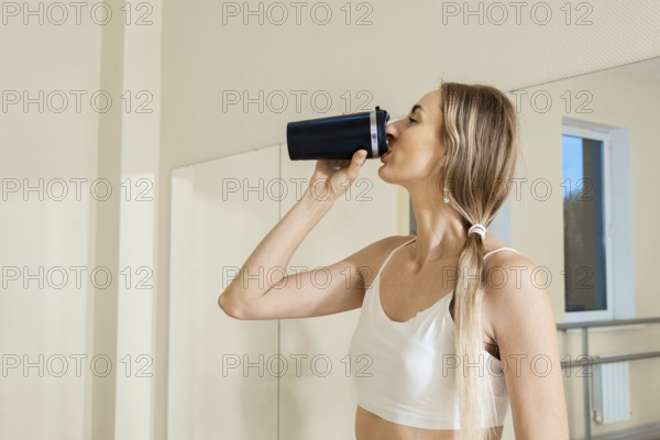 Woman enjoying a drink while standing in a fitness studio after a workout session
