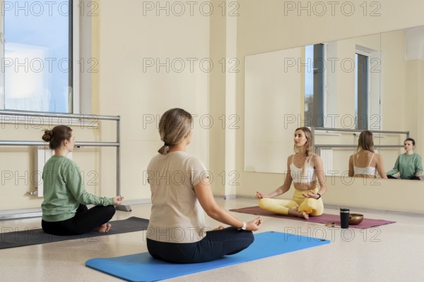 Three individuals practice meditation in a well-lit studio, focusing on relaxation. Soft mats are laid out on a smooth floor as they sit in calm postures. The atmosphere promotes mindfulness