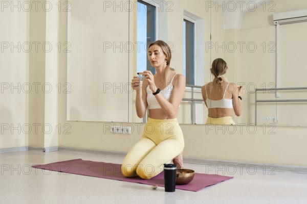In a spacious yoga studio, a woman kneels on a mat and ignites the palo santo incense stick