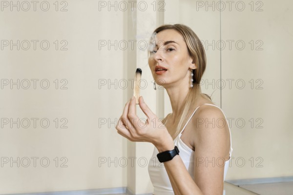 A woman with long hair is sitting calmly and gently holding an incense stick. Smoke is rising gracefully from it, creating a peaceful atmosphere, ideal for relaxation or meditation