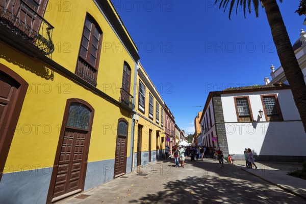 View along historic street with yellow facades and passers-by in sunny weather, UNESCO World Heritage Old Town of San Crstobal de La Laguna, La Laguna, Tenerife, Canary Islands, Spain