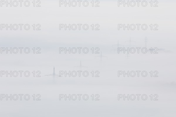 High-voltage pylons rise up from the thick sea of fog, silence and technology the silhouette of power lines in fog