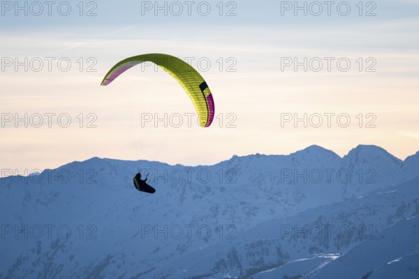Paragliders flying over snowy mountain peaks in winter in evening light, KitzbÃ¼hel Alps, Tyrol, Austria