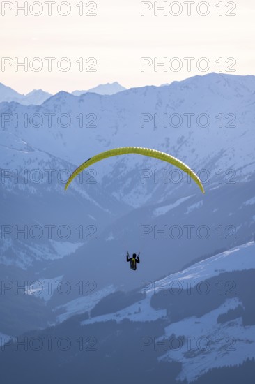 Paragliders flying over snowy mountain peaks in winter in evening light, KitzbÃ¼hel Alps, Tyrol, Austria