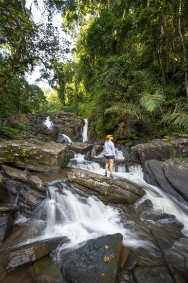 Tourist at Derema Waterfall, flows through dense vegetation, tropical rainforest in Amani Nature Forest Reserve, long exposure, Eastern Usambara Mountains, Tanga, Tanzania