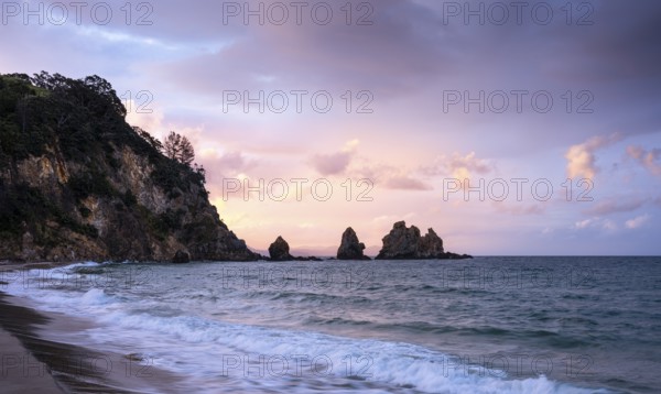 Landscape with sea, rocks and sandy beach in New Zealand in the evening at sunset. Otama Beach, Coromandel Peninsula, Waikato, New Zealand