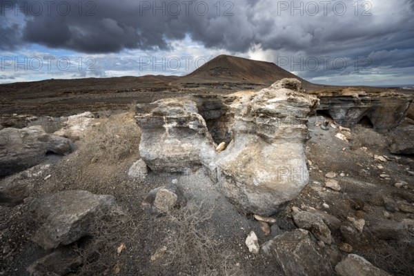 Eroded rock formations in volcanic landscape with dramatic cloudy skies, Ciudad Estratificada or Los Roferos, Antigua Rofera de Teseguite, Lanzarote, Canary Islands, Spain