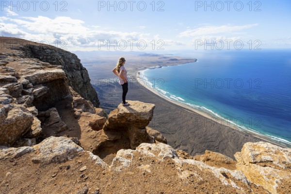 Young woman enjoying the view from the Risco de Famara cliffs to Famara beach, Playa de Famara with La Calaeta, Lanzarote, Canary Islands, Spain