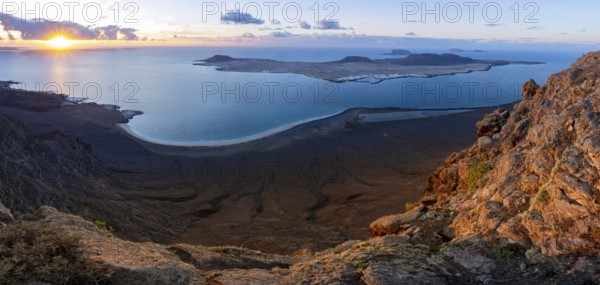 View of steep cliffs to sea and the island of La Graciosa with sun stars, Mirador del Porrito viewpoint at sunset, Lanzarote, Canary Islands, Spain