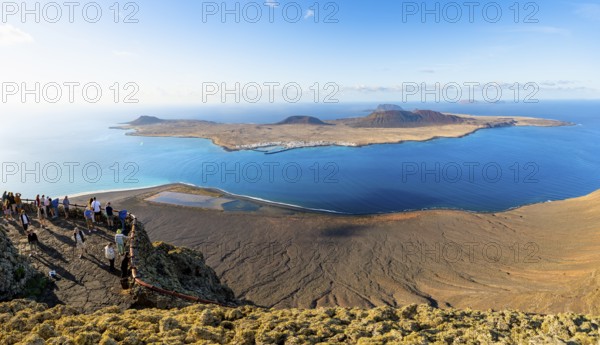 View of La Graciosa island with volcanic craters in the evening light, tourists on an observation deck at the Mirador del RÃ­o viewpoint designed by artist CÃ©sar Manrique, Lanzarote, Canary Islands, Spain