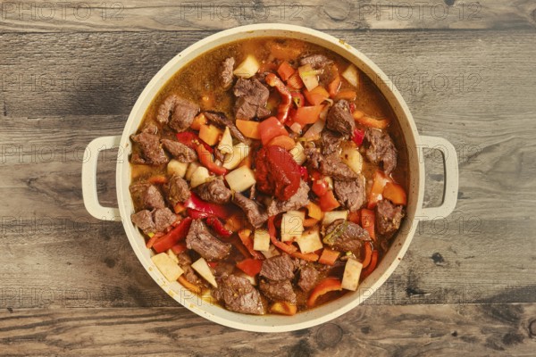 Tender beef chunks are mixed with vegetables like carrots, bell peppers and celery root in a pot. The dish simmers gently, releasing savory aromas that fill the kitchen