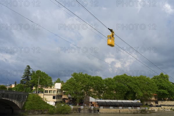 Yellow cable car crosses river, in the background a cloudy city, cable car cabin above the Rioni river, Kutaisi, Imereti region, Georgia