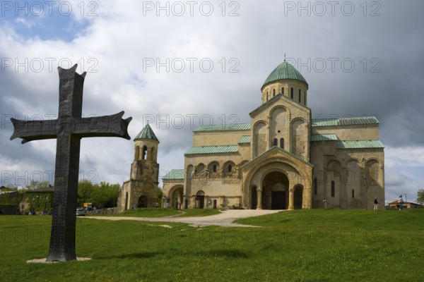 Historic church with cross in the foreground, cloudy sky surrounded by green landscape, Bagrati Cathedral, Church of the Dormition of the Most Holy Mother of God, UNESCO World Heritage Site, Kutaisi, Imereti Region, Georgia