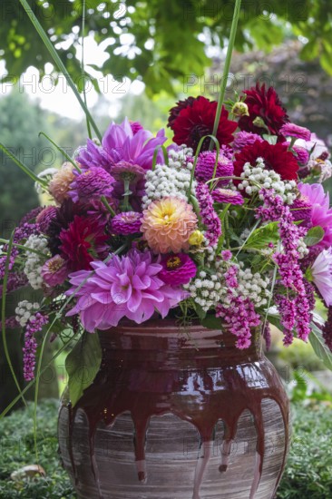 A vivid bouquet of flowers in shades of pink and red stands in a rustic vase against a green background, North Rhine-Westphalia, Germany