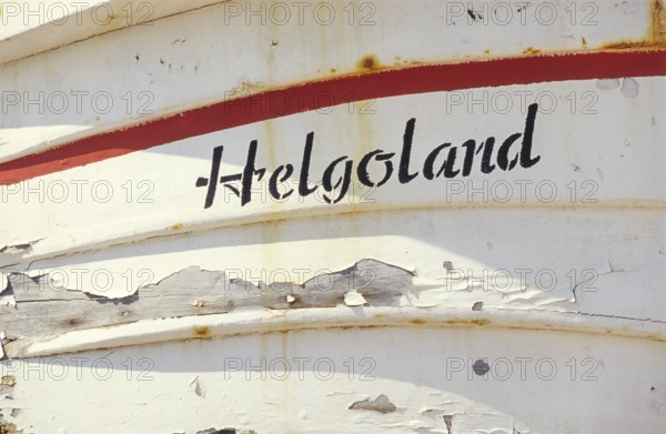 Weathered Heligoland lettering on white boat with red accents on a sunny day, bright, friendly, sunlight, peeling paint and rust spots, Börteboot oak rim and upper planks, clinker construction, traditional rowing boat, disembarkation, detail, close-up, planks, boards, painted, vintage, shabby, shabby, shabby look, shabby, tourism, travel, excursion destination, symbolic image, harbor, high-seas island of Heligoland, North Sea, Pinneberg district, Schleswig-Holstein, Germany
