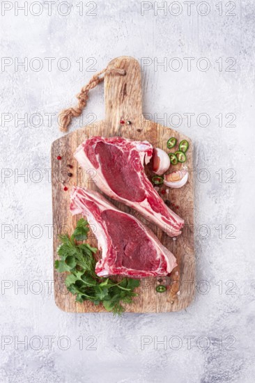 Fresh pieces of beef on the bone, on a wooden cutting board, with herbs and spices, ready for cooking in the kitchen